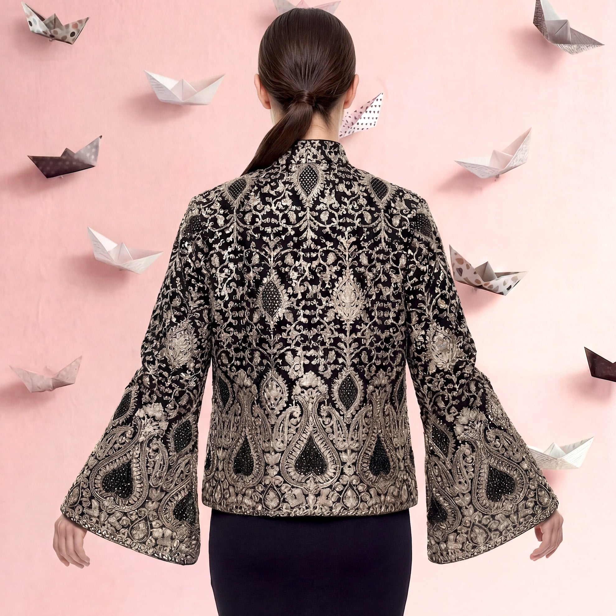 Woman wearing a patterned jacket with bell sleeves on a pink background with paper boats.